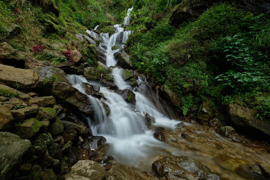 View of Jumog Putri Waterfall cascading over mossy rocks surrounded by lush tropical greenery and vibrant foliage in Tawangmangu, Karanganyar, Central Java, Indonesia.