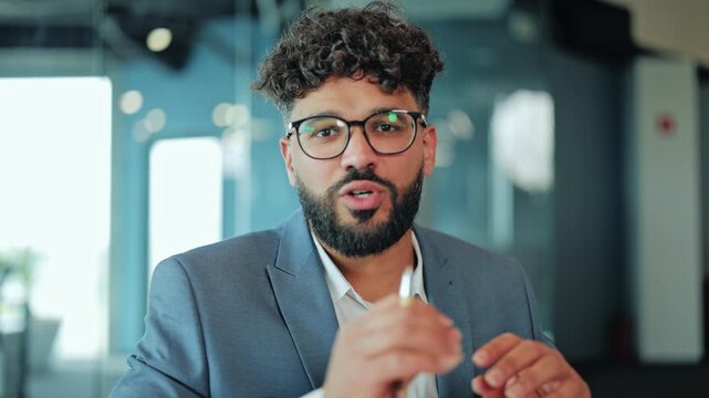 Confident Middle Eastern businessman talking during online meeting and looking at laptop web camera. Corporate leader gesturing and speaking on video conference at modern workplace.
