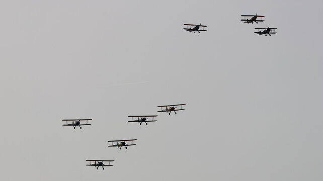 View of a formation of vintage biplanes flying through a grey overcast sky during an airshow in La Ferte-Alais, Ile-de-France, France.