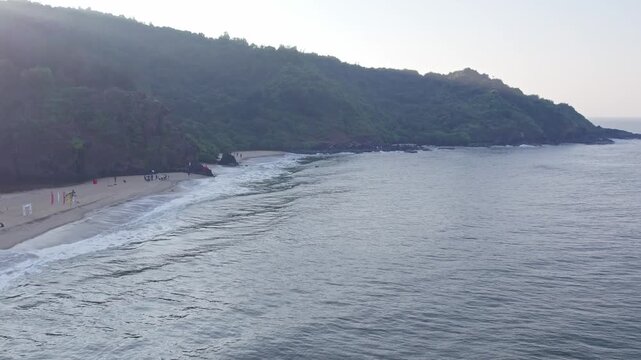 Dolly view of people enjoying beach waves with hills and scenic coastal surroundings
