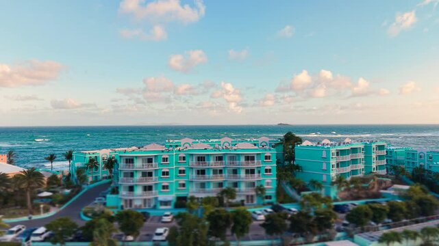 Drone view of a luxury tropical resort with bright blue buildings on Saint Martin island in the Caribbean Sea. Aerial look at beautiful seaside apartments and multi story accommodation complex.