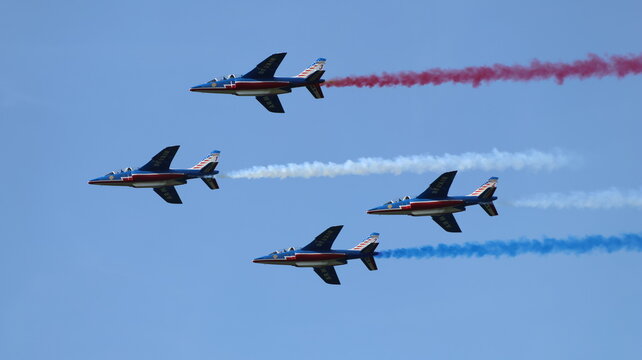 View of Patrouille de France aerobatic team flying in formation and trailing red, white, and blue smoke against a clear blue sky during an airshow La Ferte-Alais, Ile-de-France, France.