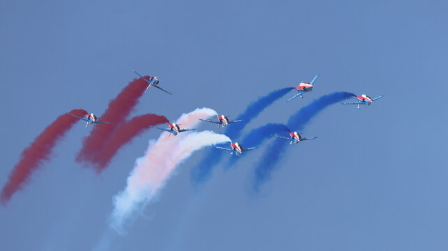 View of the Patrouille de France aerobatic team performing maneuvers with red, white, and blue smoke trails against a clear blue sky during an air show in La Ferte-Alais, Ile-de-France, France.