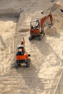 Orange Doosan compact track mini excavators operating on a sandy excavation construction site, preparing the ground for foundations.