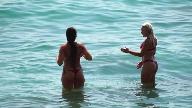 Women swimming sea, two young friends in red bikinis enjoy a conversation while standing in turquoise tropical waters on a sunny day