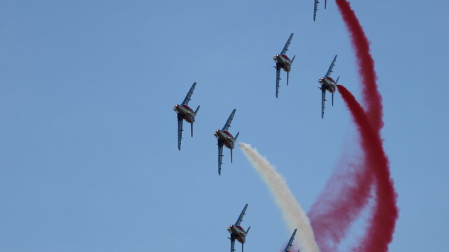 View of Patrouille de France jets performing aerobatic maneuvers with red and white smoke trails in a clear blue sky at the airshow in La Ferte-Alais, Ile-de-France, France.