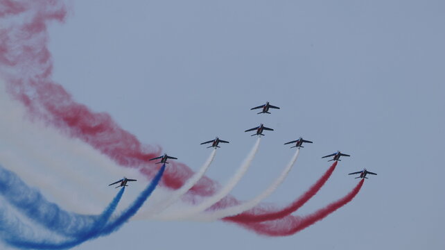 View of the Patrouille de France aerobatic team performing a formation flight with red, white, and blue smoke trails during an airshow La Ferte-Alais, Ile-de-France, France.
