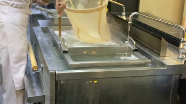 4k video footage of A chef is boiling traditional Japanese udon noodles using a large mesh strainer in a modern commercial kitchen at a restaurant.