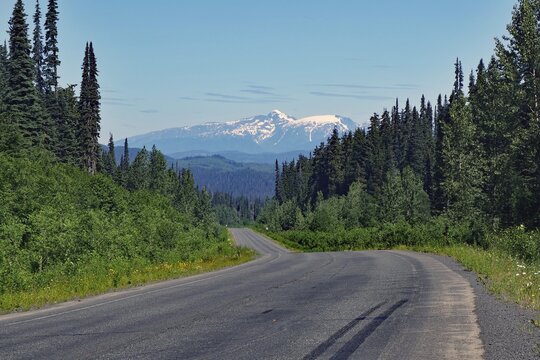 Narrow, traffic-free road leads through rugged mountain landscape, forest and snow-covered mountains, wilderness, Stewart Cassiar Highway, British Columbia, Canada