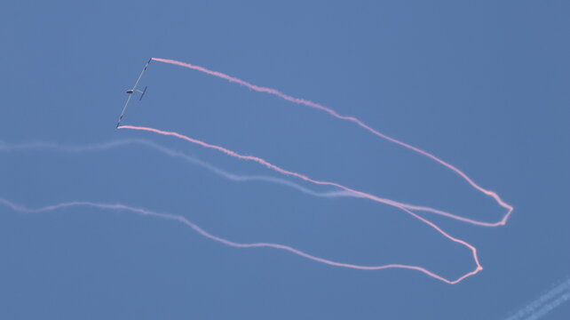View of a glider performing aerobatic maneuvers with pink smoke trails against a clear blue sky during an air show in La Ferte-Alais, Ile-de-France, France.