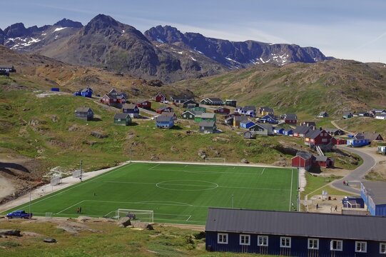 Village with colourful houses and a green football pitch surrounded by mountains and clear skies, artificial turf, Tasilaq, Greenland, Denmark