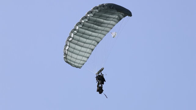 View of a paratrooper descending with a large grey parachute against a clear blue sky in La Ferte-Alais, Ile-de-France, France.