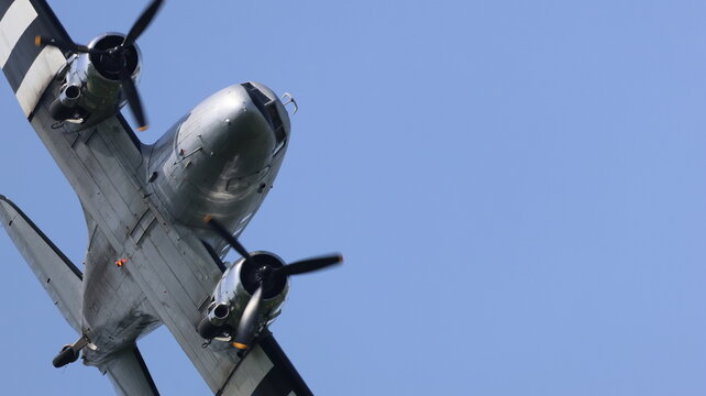 View of a vintage twin-engine propeller aircraft with invasion stripes flying against a clear blue sky in La Ferte-Alais, Ile-de-France, France.