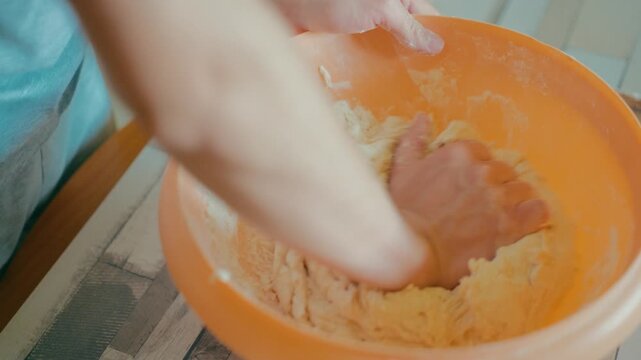 Close up shot of teenage hands kneading fresh sticky dough inside an orange bowl. Traditional bread making process, working with texture, culinary skills, cozy home kitchen lifestyle, 4k.