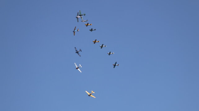 View of a formation of vintage propeller airplanes flying through a clear blue sky during an airshow in La Ferte-Alais, Ile-de-France, France.