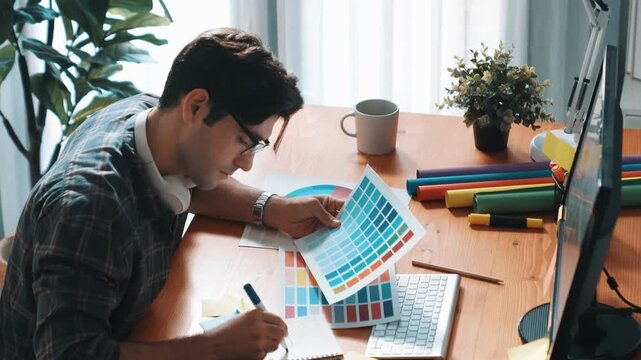 Professional designer writing and designing logo graphic at meeting. Closeup of business man working on colored palettes and writing idea on sticky notes on table with equipment and paper. Symposium.
