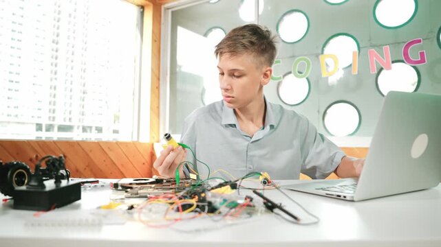 Smart happy boy inspect or learning to use electronic tool to fix car model. high school student studying about electric equipment to repair robotic machines while sitting at STEM class. Edification