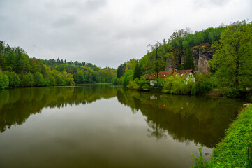 Obraz premium Pond in the Bohemian Paradise region of the Czech Republic with traditional rural farmhouses and distinctive sandstone rock formations, a hallmark of this scenic landscape.