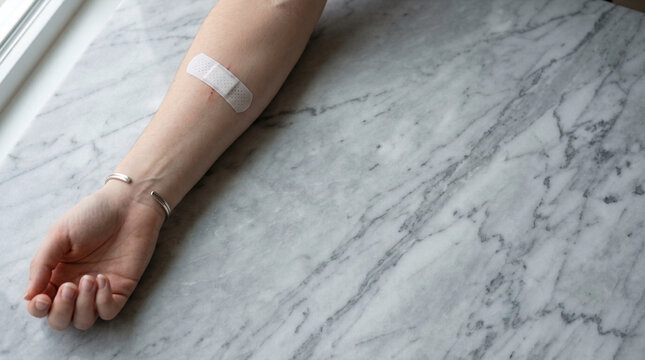 Patient arm with white bandage after blood test on white marble background