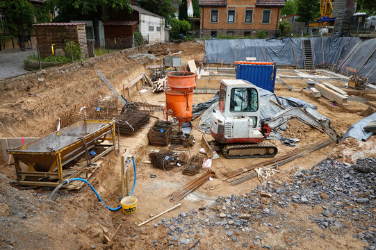 Blick in eine Baugrube f&uuml;r ein Fundament mit Minibagger Takeuchi TB 125, sowie Betonwannen, Stahlbewehrungen, Container, Planen und Bauholz in Vaihingen an der Enz, Deutschland am 04. Juni 2026