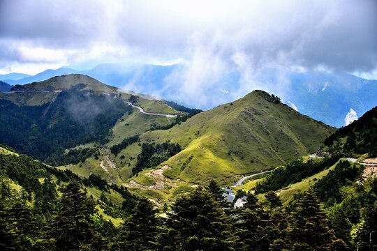Majestic green mountain peaks and winding alpine road amidst rolling clouds at Wuling, Hehuan Mountain, Taiwan.
