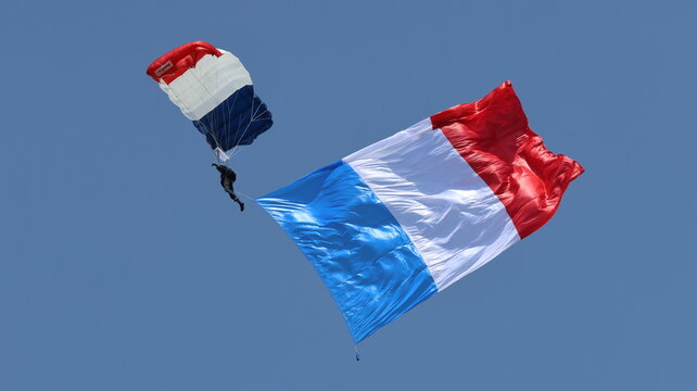 View of a parachutist descending with a large French flag against a clear blue sky in La Ferte-Alais, Ile-de-France, France.