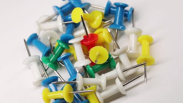 Office supplies, many multi-colored push pins, paper clips on white background, rotating in the office, close up view