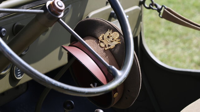 View of a vintage US Army officer service cap with a gold eagle emblem hanging on the steering wheel of an olive drab military vehicle La Ferte-Alais, Ile-de-France, France.
