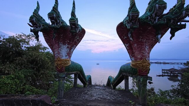 Twin naga statues framing calm sea with distant horizon at dusk