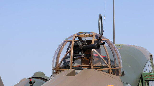View of the glass turret and machine gun of a vintage military aircraft with camouflage paint under a clear blue sky La Ferte-Alais, Ile-de-France, France.
