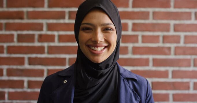 Education, face and funny with Muslim woman on brick wall background at college campus. Belief, laughing and learning with student at university for Arabic, Islamic or religious studies as scholar