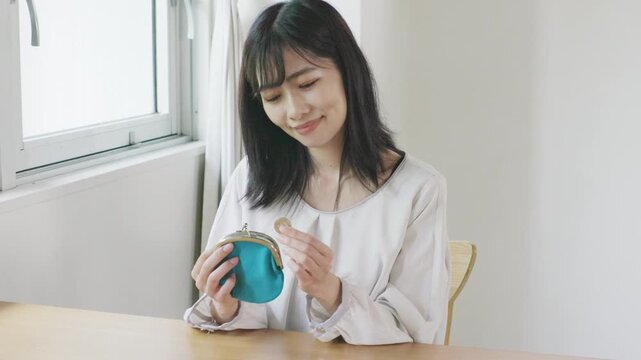 Young Asian woman smiling while taking coins from wallet at window table