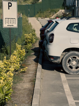 View of parked cars in a designated parking area next to a sign and lush green bushes in Sariyer, Istanbul, Turkiye.
