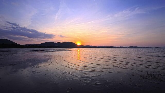 Sunset reflection across shallow tidal water beside distant mountains