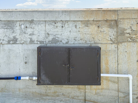 View of a dark metal utility box mounted on a weathered concrete wall with industrial pipes and a clear sky Sariyer, Istanbul, Turkiye.