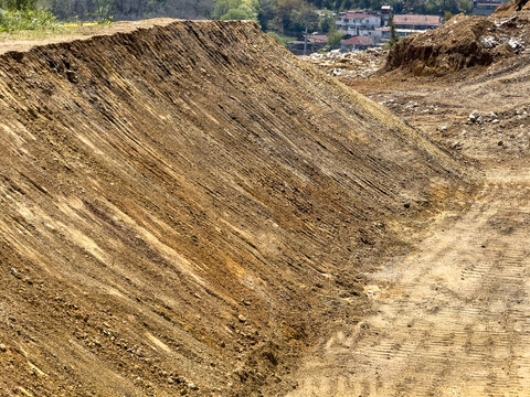 View of excavated earth and a steep dirt bank at a construction site with tire tracks and residential buildings in the background Sariyer, Istanbul, Turkiye.