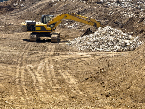View of a yellow excavator working on a construction site moving a pile of white rocks on brown earth Sariyer, Istanbul, Turkiye.
