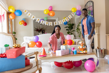 Obraz premium African American couple arranging Happy Birthday banner and balloons on coffee table in living room