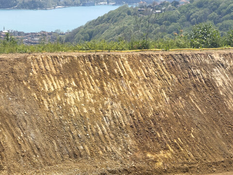 View of a steep excavated dirt embankment overlooking lush green hills and the blue waters of the Bosphorus strait in Sariyer, Istanbul, Turkiye.