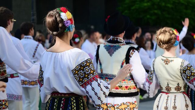 Group of young people dancing in traditional romanian folk costumes outdoors.