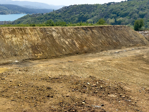 View of an excavated construction site with a large dirt embankment and green hills overlooking the water in Sariyer, Istanbul, Turkiye.