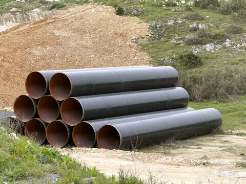 View of large black industrial pipes stacked on a construction site with green hills and excavated earth in the background Sariyer, Istanbul, Turkiye.