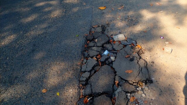 Damaged asphalt road with deep cracks and broken potholes on street surface.