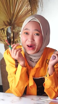 Close-up of a Muslim woman laughing when her false eyelash falls off during makeup.