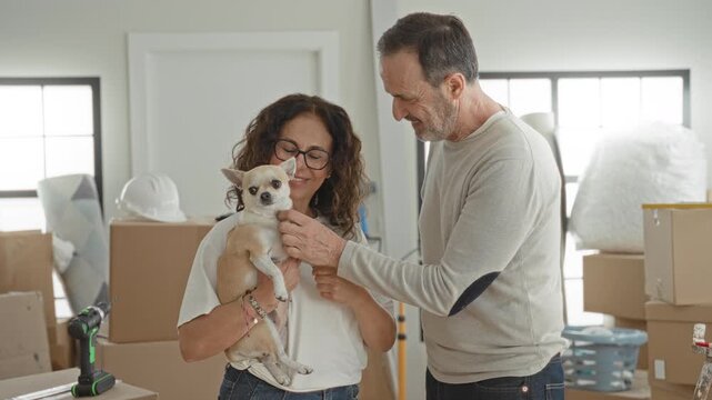 Man and woman hold small dog and stacked moving boxes in a home building; moving together contentment.