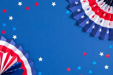 Fourth of July patriotic paper fans with American flag pattern and star confetti on blue background. 4th of July Independence Day celebration flat lay backdrop with central copy space. © prime1001