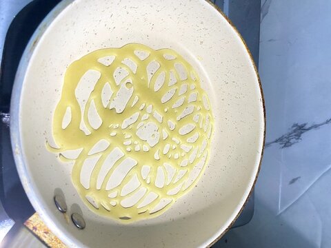 Lacy pancake roti jala cooking in a white frying pan