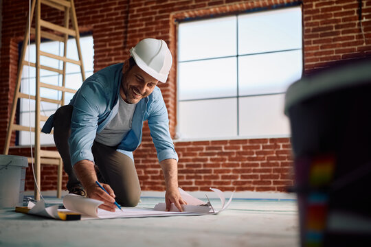 Happy architect working on blueprints during home remodeling project.
