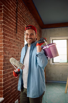 Happy man painting walls while renovating his apartment and looking at camera.