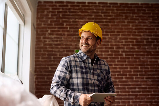 Happy construction worker using touchpad while working in renovating house.